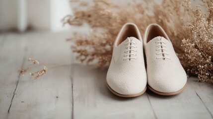 A pair of elegant beige lace-up shoes placed on a rustic wooden floor, with a minimalist background and dried plants, highlighting sophistication and simplicity.