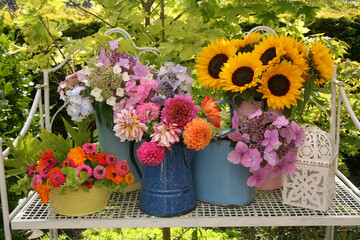Summery still life display of flowers in metal jugs and bowl on a metal bench in a garden