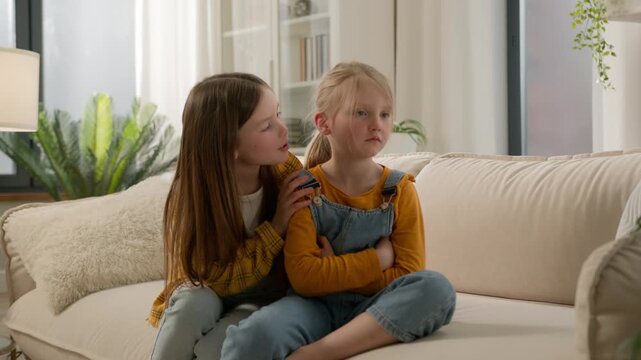 Upset sad little Caucasian children kids argument conflict. Offended girls friends ignoring boycott sisters asking forgiveness apology guilty daughters touch telling sorry sofa home friendship trouble