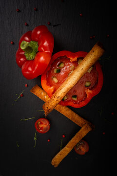 A gourmet vegetable dish: gazpacho soup in red bell peppers, garnished with basil and slices of dried bread on a black background. High quality photo