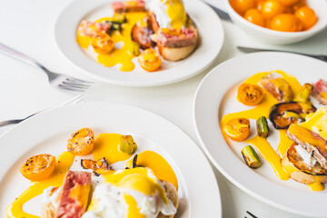 Egg Benedict with tuna, bacon, asparagus and tomatoes with hollandaise sauce on three white plates. The concept is a delicious family breakfast. Selected focus. High quality photo