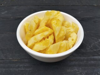 Fresh pineapple pieces in white bowl on the wooden table 