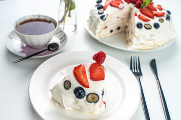 Pavlova cake or meringue dessert with berries on a white table and a cup of black tea. Close-up, focus selected. High quality photo