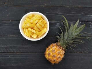 Fresh pineapple pieces in white bowl on the wooden table 