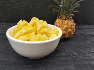 Fresh pineapple pieces in white bowl on the wooden table 