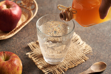 Pouring apple cider vinegar into a glass of water, with fresh red apples in the background