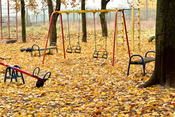 Yellow fallen leaves carpeted the ground around the carousels at a children's playground in autumn.