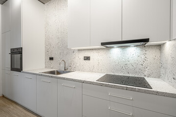 A modern kitchen with white cabinets, marble countertops, an integrated oven, a sleek stovetop, and a minimalist design, featuring bright lighting and a clean, contemporary aesthetic.
