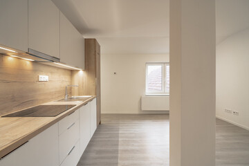 Obraz premium A modern kitchen with light wood countertops, white cabinets, a stove, and a sink, adjacent to an open area with large windows and light wood flooring.