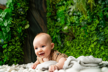 Baby playing on soft blanket in a green indoor garden. A happy baby enjoys tummy time on a cozy blanket surrounded by vibrant greenery.