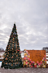 Christmas tree decorated with gifts at an outdoor event in winter. A large Christmas tree adorned with ornaments and surrounded by colorful gift boxes.