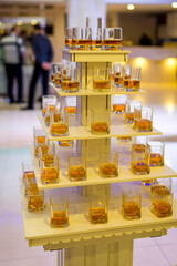 Stacked whiskey glasses arranged on a display in a banquet hall. A tiered display holds numerous glasses filled with whiskey at an event venue.