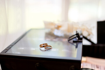 Wedding rings placed elegantly on a glass box near floral decor. Two wedding rings resting on a glass surface, surrounded by soft wedding decorations.