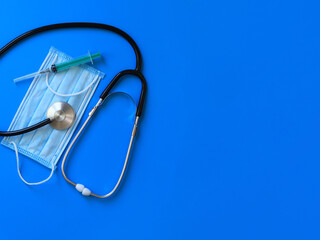 Stethoscope, protective medical mask and syringe on a blue background. Medical internet banner with copy space. Healthcare concept. Items related to the outbreak of a viral pandemic. Top view