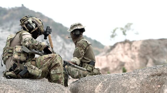 A group of military men in combat gear patrol in the middle of a desert and tropical jungle. Soldiers in full combat gear in dry weather conditions assemble and march on a mission.