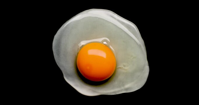 The process of cooking fried eggs in a frying pan in real time on a completely black background, top view.