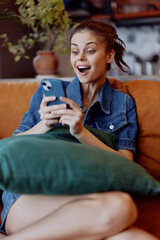Obraz premium Young woman relaxing on couch with phone in hand and pillow in front of her in cozy home environment