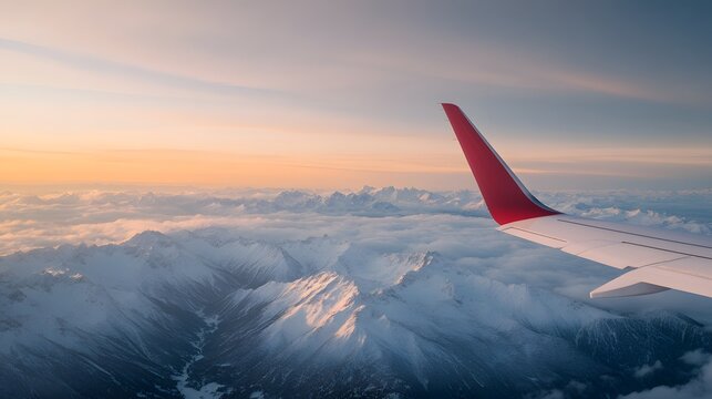 A stunning aerial view of snow-capped mountains at sunset, captured from an airplane window with a colorful wing in the foreground.