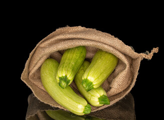 Four ripe zucchini in a jute bag, macro, isolated on black background.