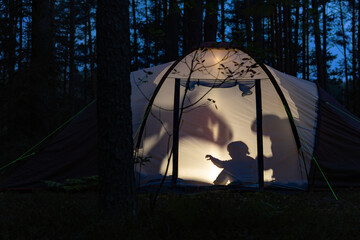 Children making shadow puppets in a camping tent at night