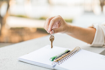 a hand holding a house key above a notebook for a new house by a realtor