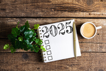 New year resolutions 2025 on desk. 2025 goals list with notebook, coffee cup, plant on wooden table. Resolutions, plan, goals, action, checklist, idea concept. New Year 2025 resolutions, copy space