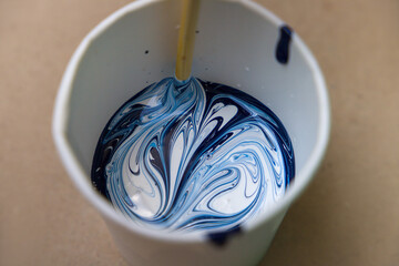 Mixing the paint by using the mixing stick. Blue and white acrylic paints.