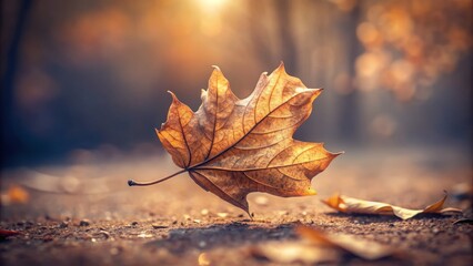 A solitary, fragile dry leaf floats gently through the autumn air, its delicate edges curled, against a soft, blurred background of muted earth tones.