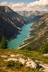 The turquoise waters of Lake Livigno in Italy stretch through the valley, flanked by towering mountains under the golden light of sunset.