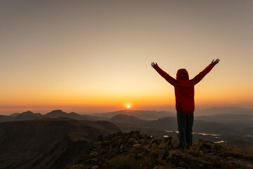 Fototapeta premium A person in a red jacket is standing on a mountain top