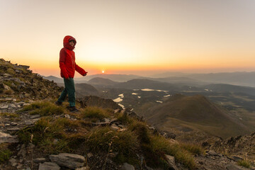 A person in a red jacket is walking on a mountain top