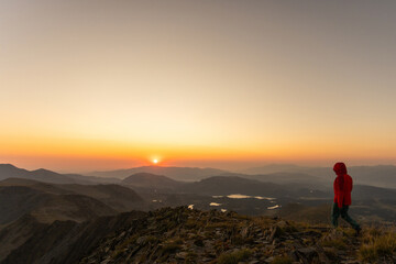 A person is walking on a mountain top at sunset