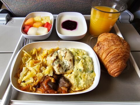 Airplane meal featuring rice, vegetables, croissant, fruit cup, and yogurt served during a midday flight
