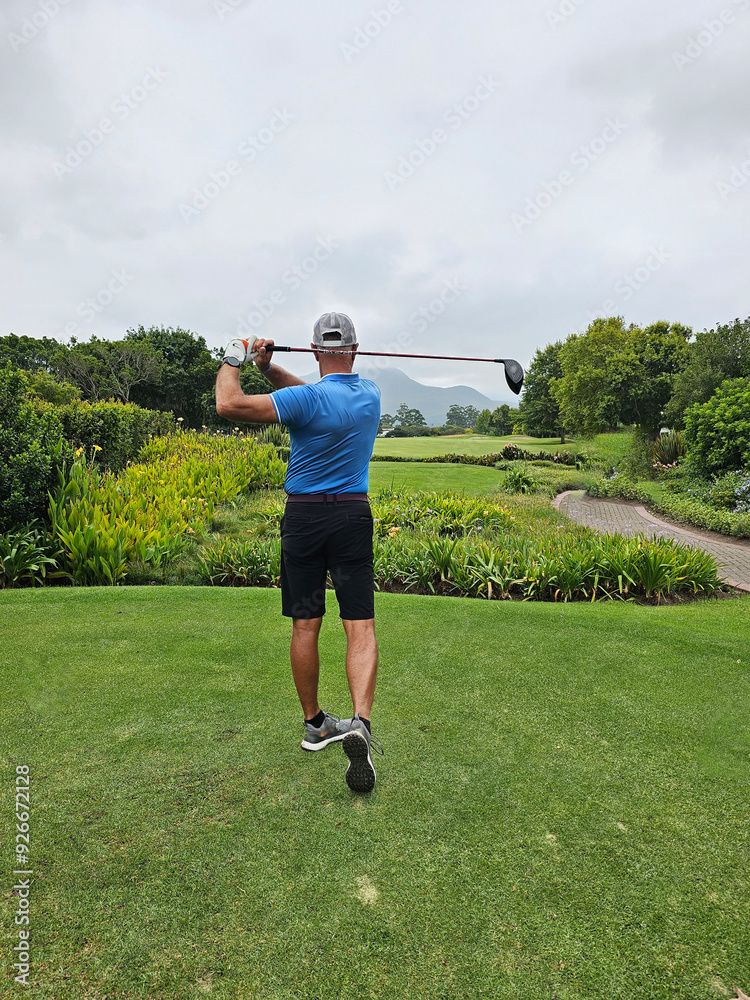 Wall mural golfer swings a driver on a lush green course in overcast weather