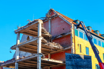 Building is being demolished in the city. Crane operates on a building undergoing demolition, showcasing the construction process in action