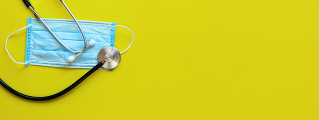 Stethoscope and protective medical mask on a yellow background. Medical internet banner with copy space. Healthcare concept. Items related to the outbreak of a viral pandemic. Top view