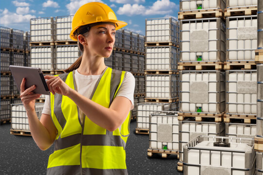 Woman logistics specialist. Street warehouse with IBC containers. Petroleum products storage area. Tanks for transporting liquid products. Woman with e-tablet recalculates IBC. Storekeeper in uniform