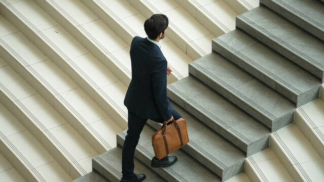Top view of smart business man walking up stairs with bag in the hand. Professional project manager climb up the stair and going to workplace. Increasing skill, getting promotion, traveling. Exultant. - Powered by Adobe