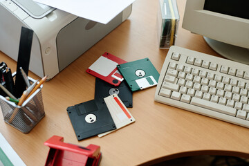 Overhead view of a retro workstation featuring scattered floppy disks, keyboard, pencil holder with...