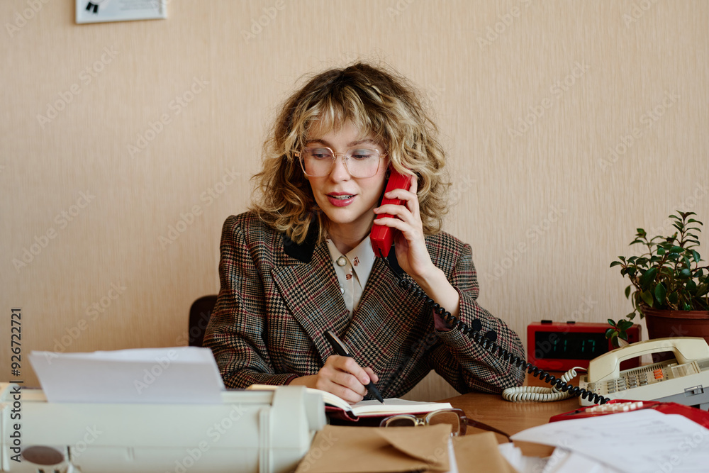 Aufkleber portrait of woman speaking on phone while writing down notes at her desk in an office setting with p