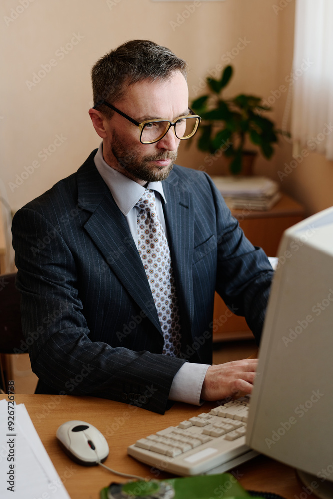 Poster businessman working on desktop computer in office, wearing suit and glasses while focusing on task, 