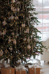 A Christmas tree with many ornaments and lights. The tree is surrounded by presents and a chair