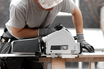 A young man is sawing a board with an electric saw.