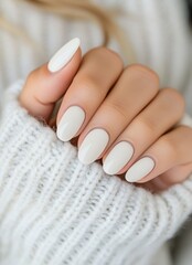 Elegant white nail design showcased with a cozy knitted sweater in a warm indoor setting