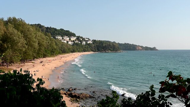 Beautiful view of the Nai Thon Beach in Phuket, Thailand. Tourists are relaxing at the beach. Green trees are standing at the beachfront.