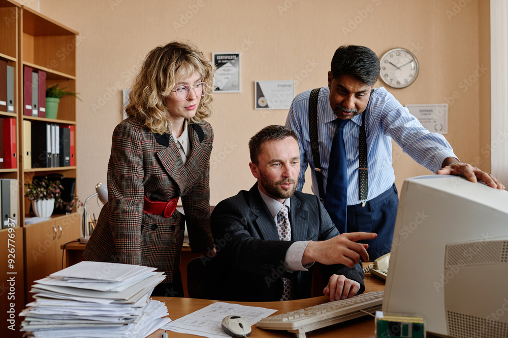 Aufkleber Three colleagues of diverse backgrounds collaborating on business project in office setting with computer and paperwork present on desk
