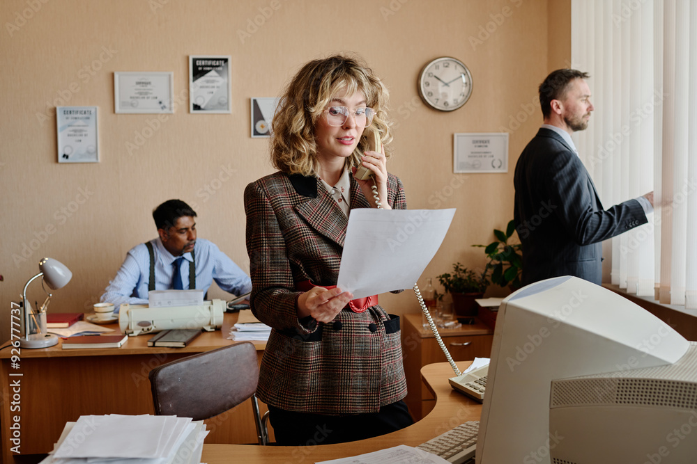 Poster Diverse business team members performing tasks in office workspace, with some looking at documents and using phones in coordinated manner