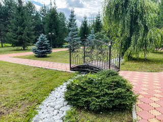 Explore a tranquil garden pathway that showcases a delightful bridge, meticulously trimmed shrubs,...
