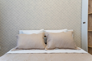 In the cozy bedroom, there is a beautifully designed bed that features a stylish white headboard and soft, comfortable beige pillows, creating an inviting and relaxing atmosphere in the space