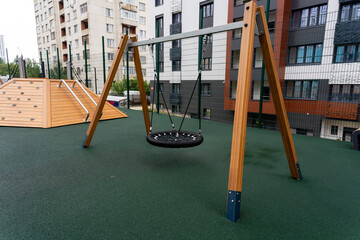 There is a swing set located in a vibrant playground, which is situated right in front of a large building, providing a wonderful area for outdoor play and recreation activities for children